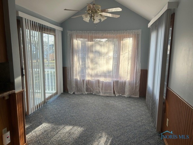 empty room with carpet flooring, a ceiling fan, a wainscoted wall, and vaulted ceiling