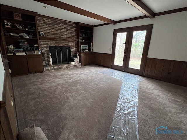 unfurnished living room featuring carpet flooring, a wainscoted wall, and beam ceiling
