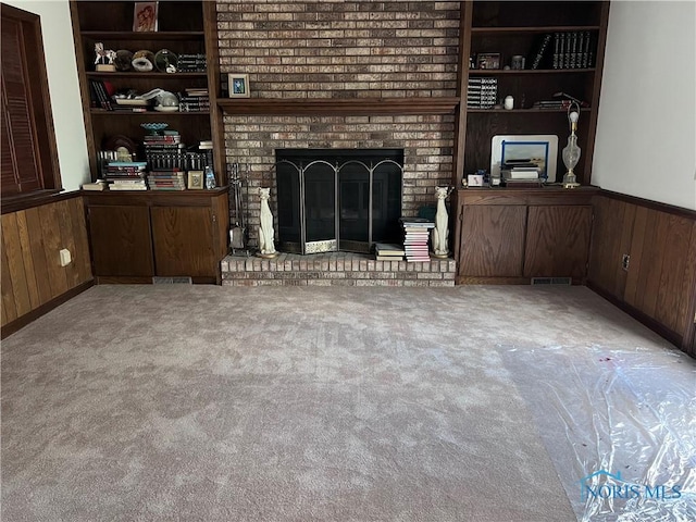 unfurnished living room featuring built in features, a wainscoted wall, a fireplace, and wooden walls