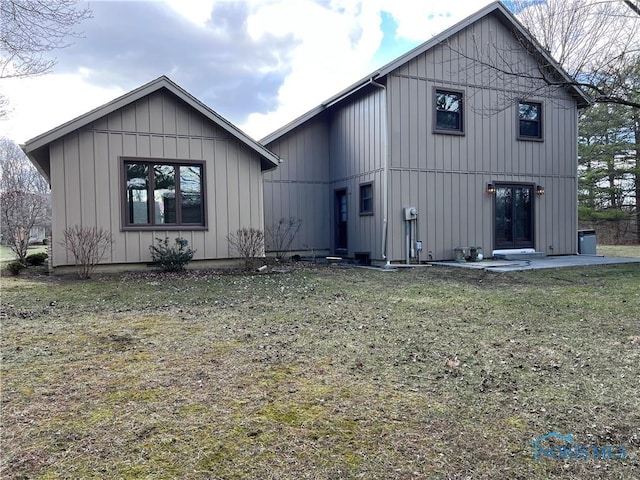 back of house with board and batten siding, a patio, and a lawn