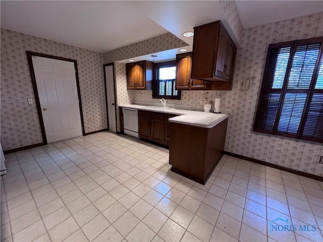 kitchen with light countertops, a sink, white dishwasher, baseboards, and wallpapered walls