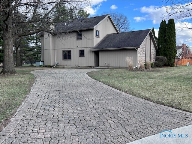 back of property featuring a lawn, decorative driveway, and roof with shingles