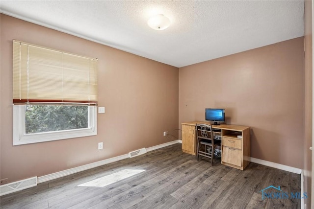 unfurnished office with baseboards, a textured ceiling, visible vents, and wood finished floors
