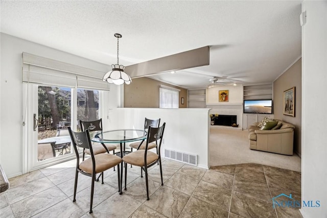 carpeted dining space with a fireplace, a textured ceiling, visible vents, and a ceiling fan