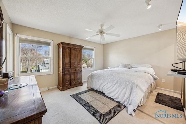 bedroom featuring light carpet, baseboards, a textured ceiling, and a ceiling fan