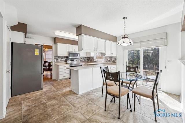 kitchen featuring light countertops, tasteful backsplash, appliances with stainless steel finishes, a peninsula, and white cabinets