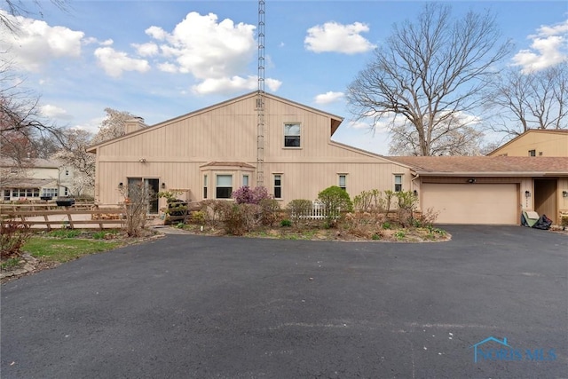view of front of home with a chimney, an attached garage, aphalt driveway, and fence