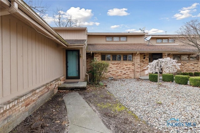 property entrance featuring brick siding and a shingled roof