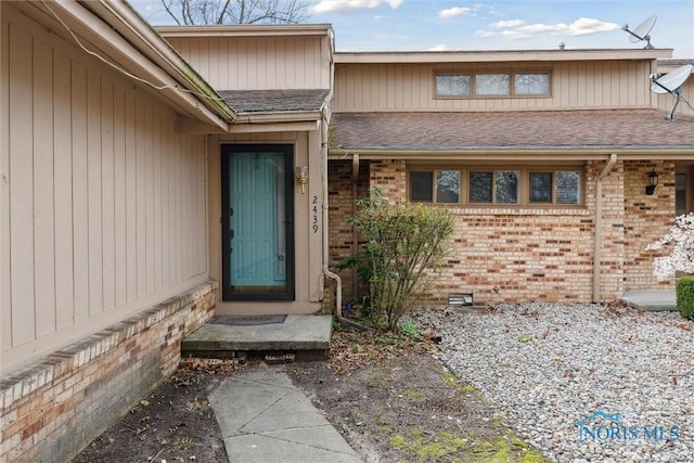 doorway to property with brick siding and a shingled roof