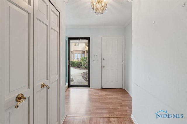 entryway with light wood finished floors, baseboards, ornamental molding, and an inviting chandelier