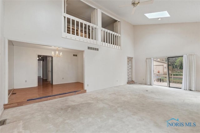 unfurnished living room with visible vents, a skylight, a high ceiling, and carpet