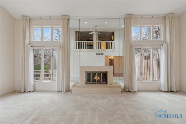 unfurnished living room with a glass covered fireplace, carpet floors, visible vents, and a ceiling fan