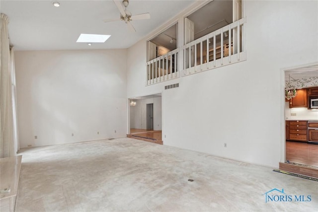 unfurnished living room with high vaulted ceiling, a skylight, ceiling fan, carpet flooring, and visible vents