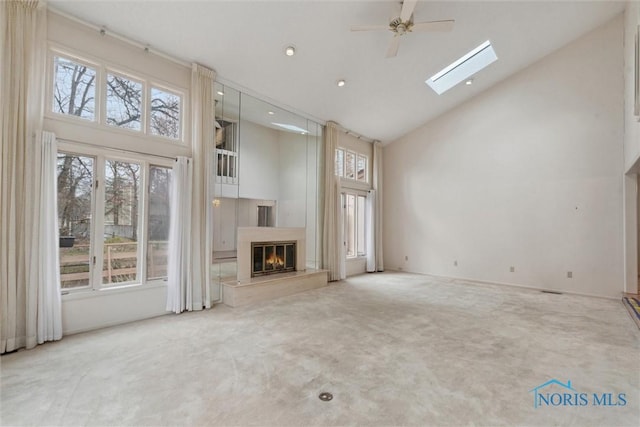 unfurnished living room featuring carpet flooring, a glass covered fireplace, a skylight, ceiling fan, and high vaulted ceiling