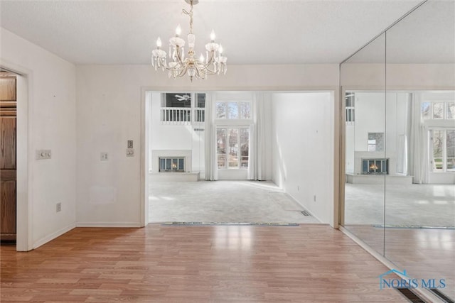 unfurnished dining area with plenty of natural light, wood finished floors, a glass covered fireplace, and a chandelier
