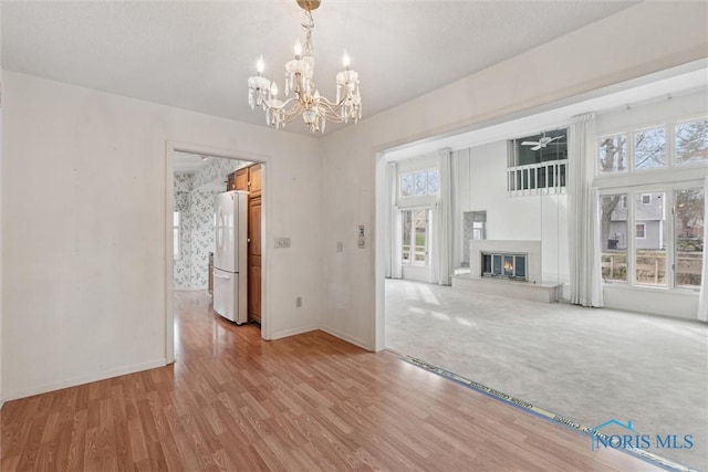 unfurnished living room featuring plenty of natural light, baseboards, a glass covered fireplace, and light wood-style floors