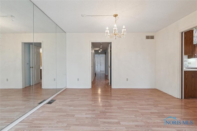 interior space featuring baseboards, light wood-style flooring, visible vents, and an inviting chandelier