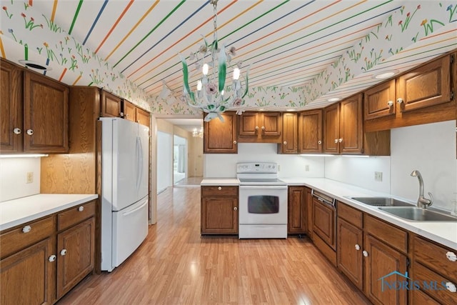 kitchen featuring brown cabinetry, wallpapered walls, a sink, and white appliances