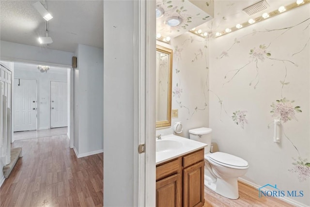 bathroom with wood finished floors, vanity, baseboards, toilet, and visible vents