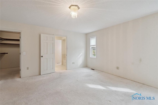 unfurnished bedroom with carpet floors, ensuite bath, and a spacious closet
