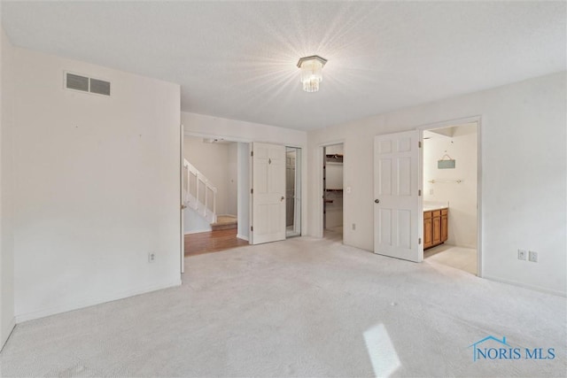 unfurnished bedroom with visible vents, light carpet, ensuite bath, a closet, and baseboards