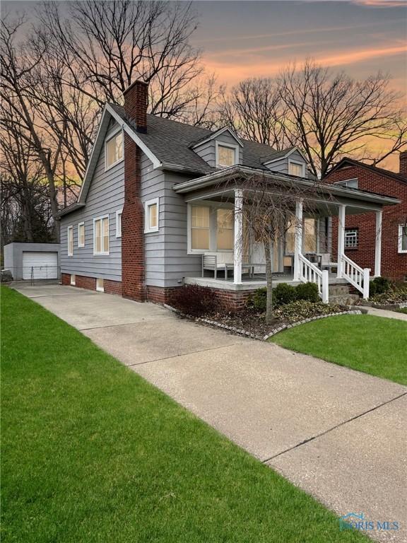 view of front facade featuring an outdoor structure, a porch, a front yard, a chimney, and driveway