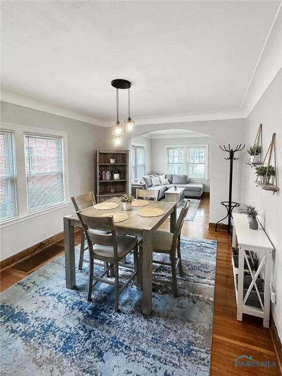 dining space featuring arched walkways, baseboards, ornamental molding, and wood finished floors