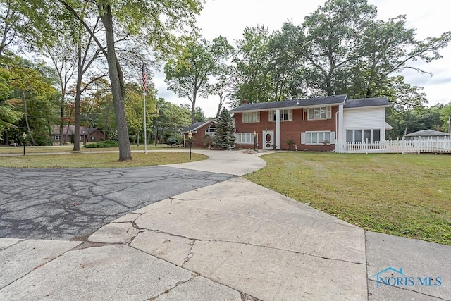 split foyer home featuring a front lawn, brick siding, and aphalt driveway