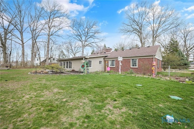 rear view of house featuring a chimney, brick siding, fence, and a lawn