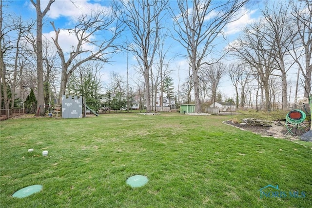 view of yard featuring fence, a playground, and an outdoor structure