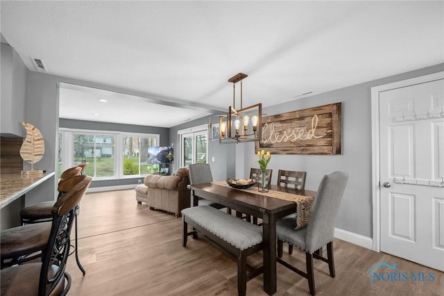 dining space featuring wood finished floors, baseboards, visible vents, and a notable chandelier