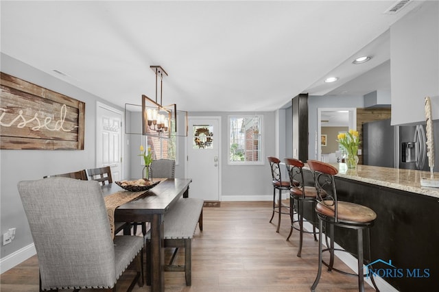 dining area with wood finished floors, baseboards, visible vents, and a notable chandelier