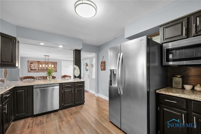 kitchen featuring light wood-type flooring, appliances with stainless steel finishes, light stone counters, baseboards, and a notable chandelier