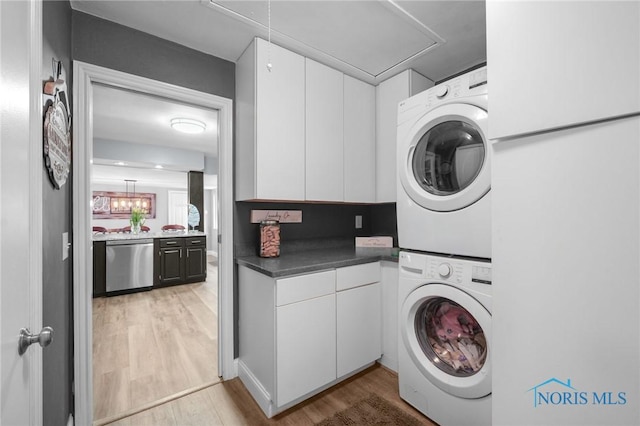 laundry area featuring light wood-style floors, stacked washer and dryer, attic access, and cabinet space