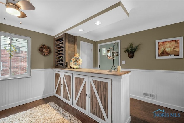 bar with a ceiling fan, dark wood finished floors, wainscoting, and visible vents