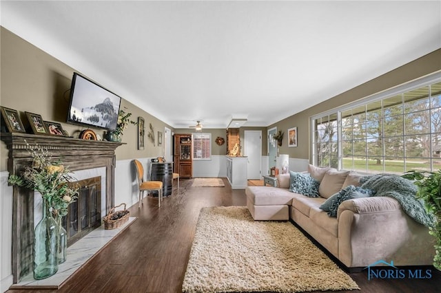 living room featuring dark wood-style floors, a fireplace, wainscoting, and a ceiling fan