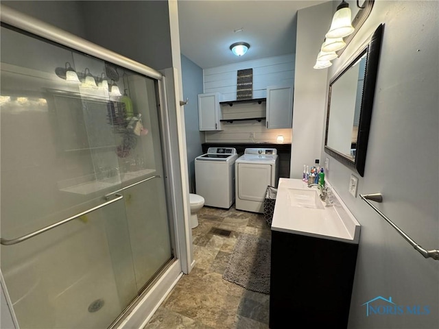 bathroom featuring a stall shower, toilet, vanity, stone finish floor, and washer and dryer