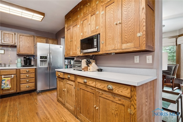 kitchen featuring light countertops, light wood-type flooring, stainless steel appliances, a sink, and brown cabinetry