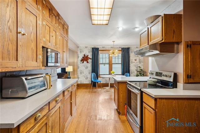 kitchen with under cabinet range hood, light countertops, wallpapered walls, and appliances with stainless steel finishes