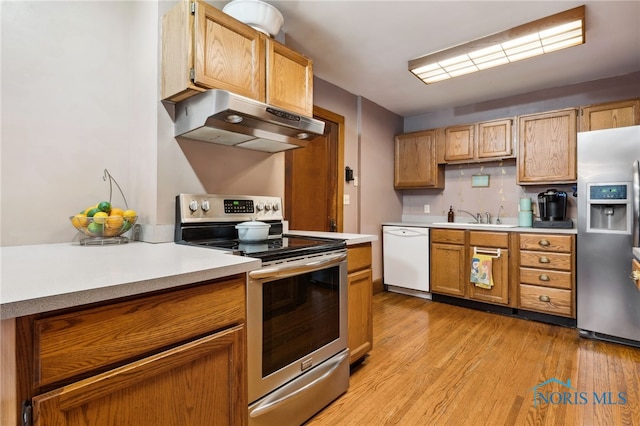 kitchen with light countertops, appliances with stainless steel finishes, under cabinet range hood, a sink, and light wood-type flooring