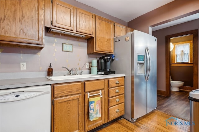 kitchen with light countertops, a sink, light wood-style floors, stainless steel fridge with ice dispenser, and white dishwasher