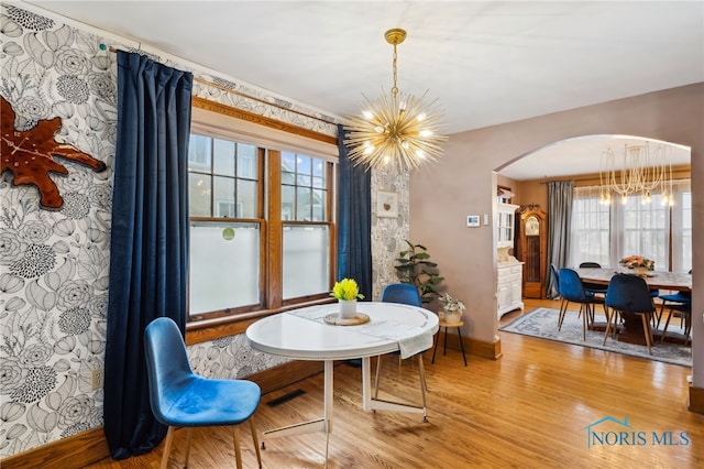 dining area with arched walkways, baseboards, wood finished floors, and a chandelier