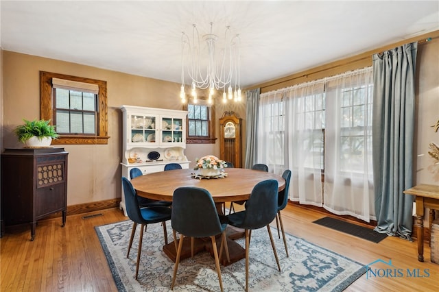 dining area with baseboards, an inviting chandelier, and light wood-type flooring