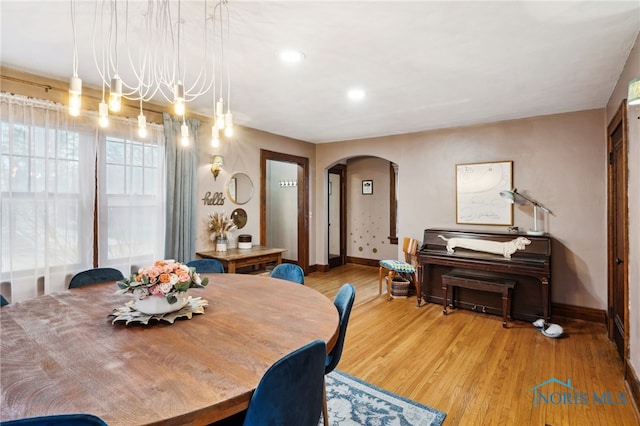 dining space featuring arched walkways, baseboards, light wood finished floors, and recessed lighting