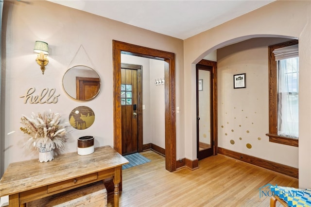 foyer featuring arched walkways, baseboards, and light wood-type flooring