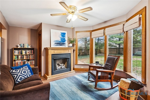 sitting room with a fireplace with raised hearth, wood finished floors, and a ceiling fan