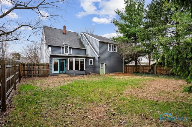 rear view of property with a fenced backyard, a yard, and a chimney