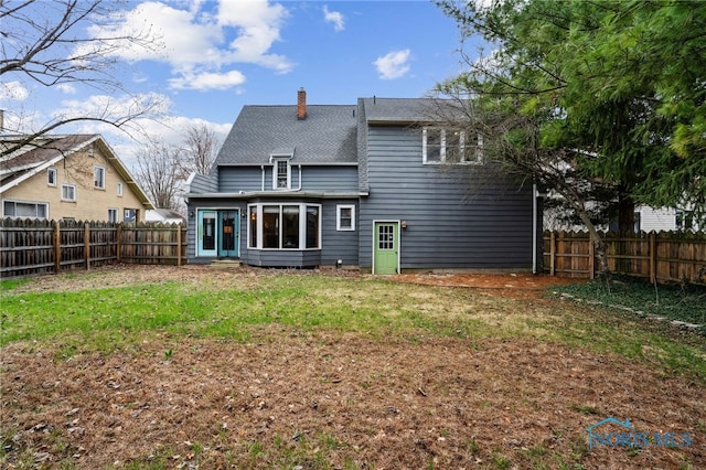 back of house with a chimney, a fenced backyard, entry steps, a shingled roof, and a lawn