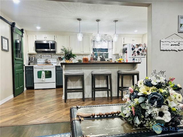 kitchen featuring a kitchen breakfast bar, tasteful backsplash, white appliances, hardwood / wood-style flooring, and pendant lighting