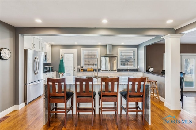 3114 Gleneagle Dr, Findlay, OH 45840 - kitchen featuring wall chimney range hood, a kitchen breakfast bar, decorative columns, appliances with stainless steel finishes, and wood finished floors